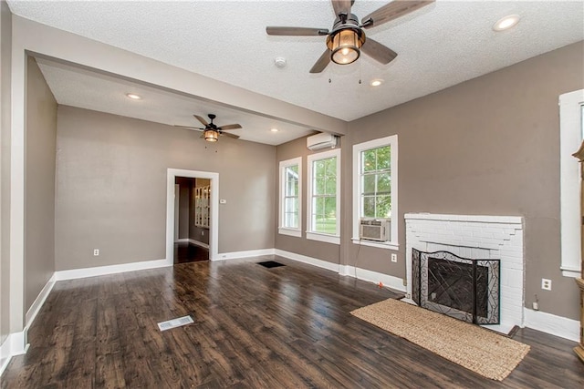 unfurnished living room with a brick fireplace, a textured ceiling, a wall mounted air conditioner, and dark wood-type flooring