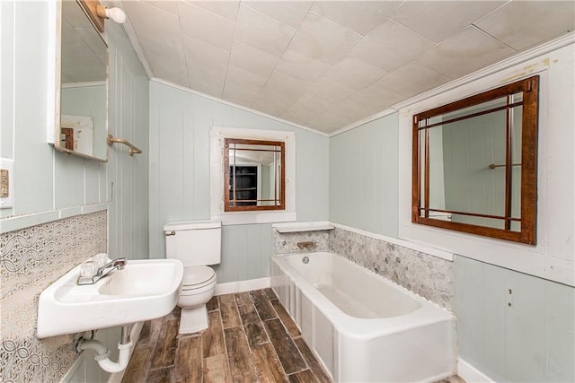 bathroom with a bathtub, hardwood / wood-style floors, vaulted ceiling, wooden walls, and toilet