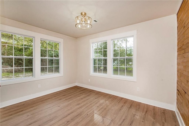 unfurnished room featuring light hardwood / wood-style floors, wood walls, and a chandelier