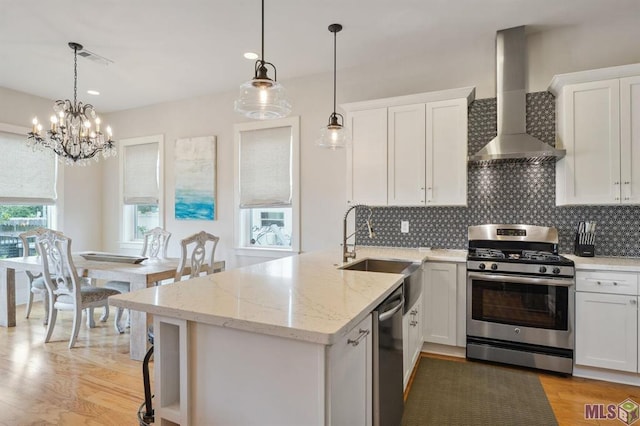 kitchen with wall chimney exhaust hood, light hardwood / wood-style flooring, a notable chandelier, stainless steel appliances, and white cabinets