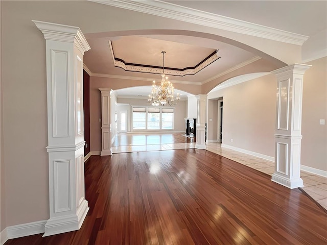 unfurnished living room with a notable chandelier, ornamental molding, wood-type flooring, and decorative columns