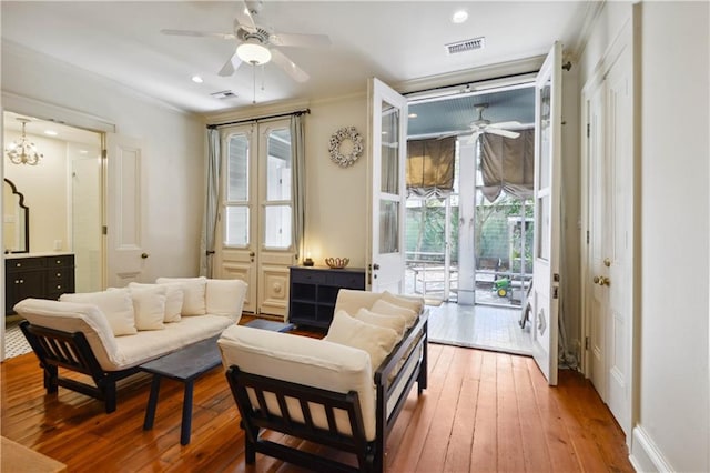 living room with ceiling fan with notable chandelier, hardwood / wood-style flooring, and ornamental molding