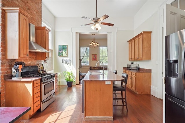 kitchen featuring an island with sink, sink, wall chimney exhaust hood, hardwood / wood-style flooring, and stainless steel appliances