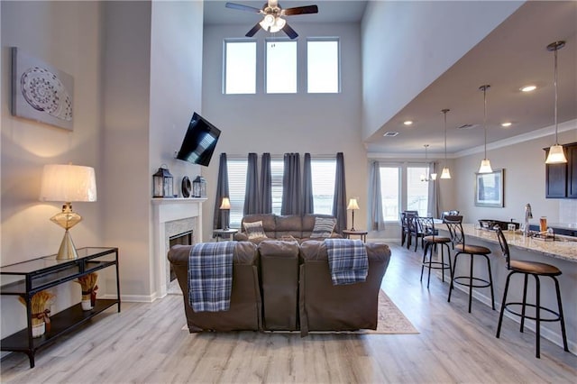 5572 Wake Reserve Rd, Slidell, LA 70461 - living room featuring light wood-style flooring, a ceiling fan, a glass covered fireplace, a high ceiling, and baseboards