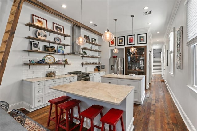 kitchen with a breakfast bar, backsplash, dark hardwood / wood-style flooring, pendant lighting, and a center island with sink