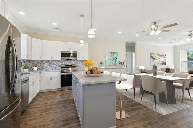 kitchen featuring ceiling fan, white cabinets, hanging light fixtures, dark wood-type flooring, and stainless steel appliances