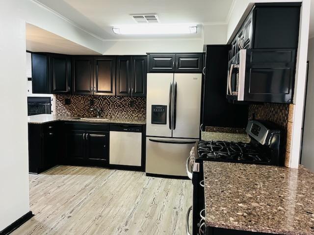 kitchen with sink, dark stone countertops, stainless steel appliances, light hardwood / wood-style floors, and backsplash