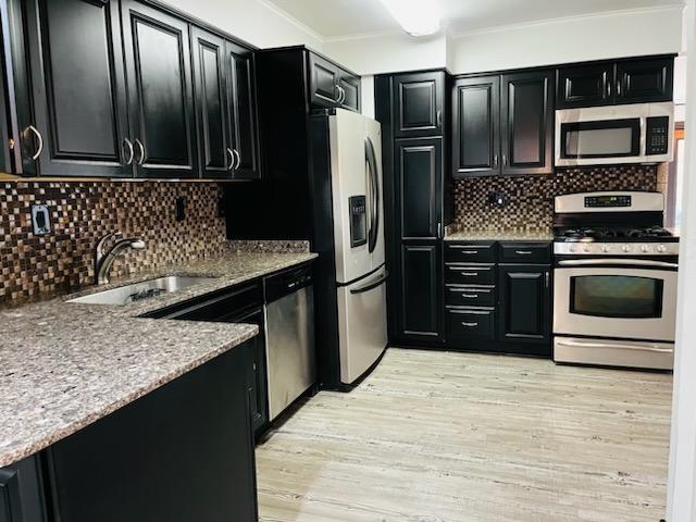 kitchen featuring appliances with stainless steel finishes, sink, decorative backsplash, light stone counters, and light wood-type flooring