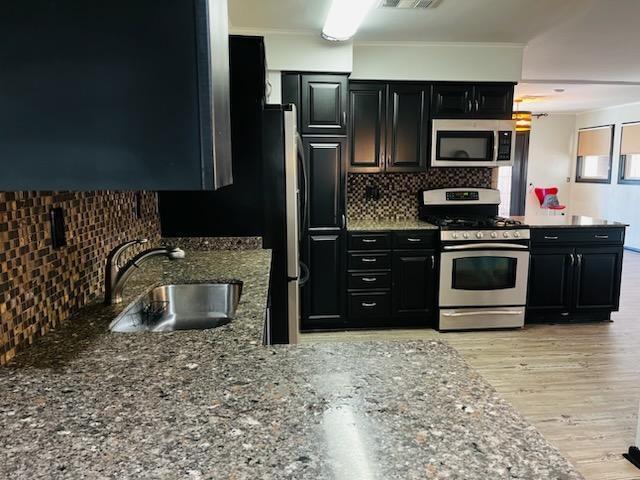 kitchen with sink, light hardwood / wood-style flooring, appliances with stainless steel finishes, stone countertops, and decorative backsplash