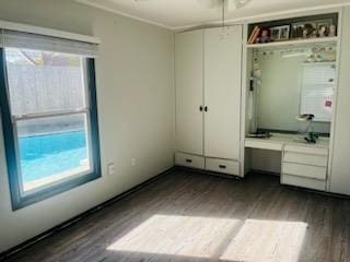 unfurnished bedroom with crown molding, dark wood-type flooring, and built in desk