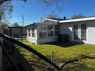 back of property with french doors, a sunroom, central AC, and a lawn