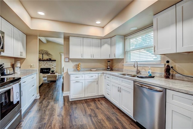 kitchen with a stone fireplace, appliances with stainless steel finishes, dark wood-type flooring, and white cabinetry