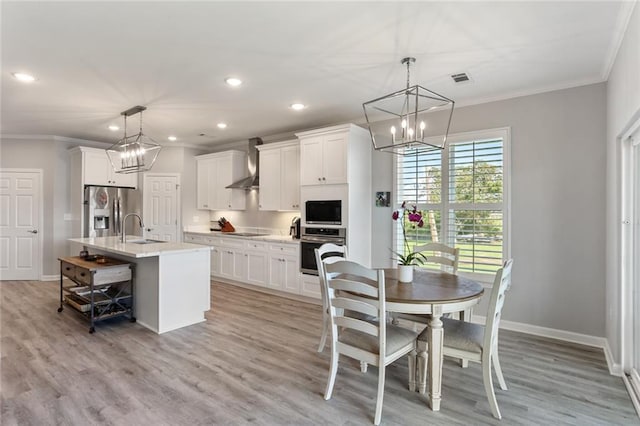 kitchen with white cabinets, hanging light fixtures, stainless steel fridge, a kitchen island with sink, and wall chimney range hood