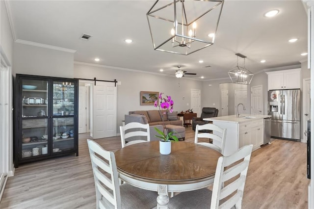 dining area featuring a barn door, ceiling fan with notable chandelier, sink, and light hardwood / wood-style flooring