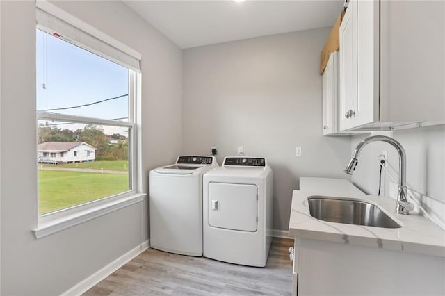 laundry room with cabinets, light wood-type flooring, separate washer and dryer, and sink