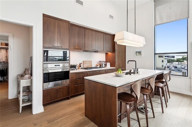 kitchen featuring an island with sink, appliances with stainless steel finishes, hanging light fixtures, and light hardwood / wood-style flooring