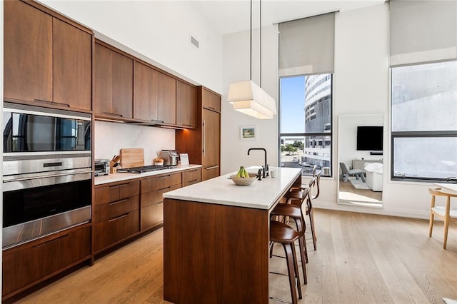 kitchen featuring appliances with stainless steel finishes, a kitchen bar, light hardwood / wood-style flooring, decorative light fixtures, and a kitchen island with sink