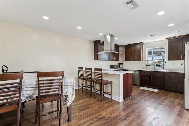 kitchen with dark brown cabinets, wall chimney exhaust hood, dark hardwood / wood-style floors, and a breakfast bar