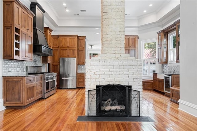 kitchen featuring wine cooler, premium range hood, light hardwood / wood-style flooring, appliances with stainless steel finishes, and crown molding