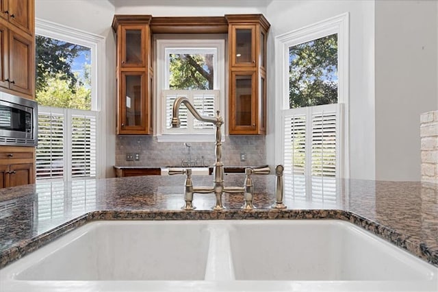 kitchen featuring dark stone counters, stainless steel microwave, and sink