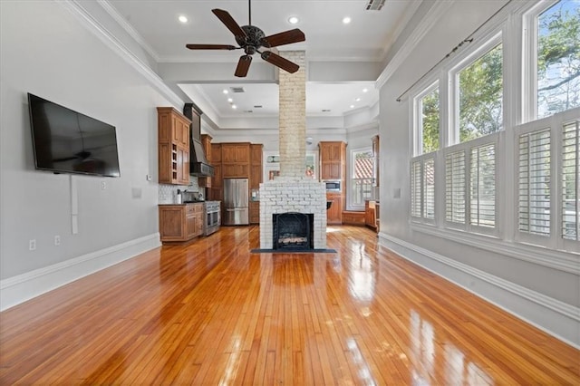 unfurnished living room with ceiling fan, light hardwood / wood-style floors, a fireplace, crown molding, and ornate columns