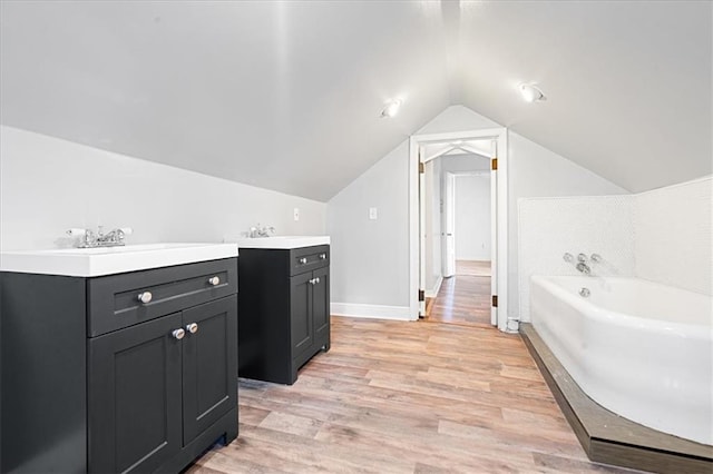 bathroom with vanity, hardwood / wood-style flooring, lofted ceiling, and a tub