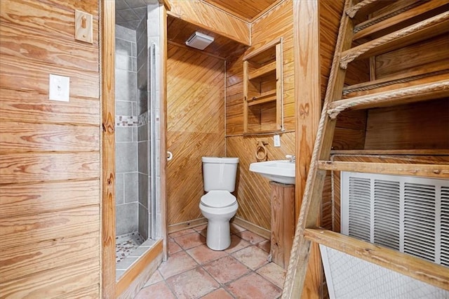 bathroom with sink, tiled shower, wooden walls, tile patterned floors, and toilet