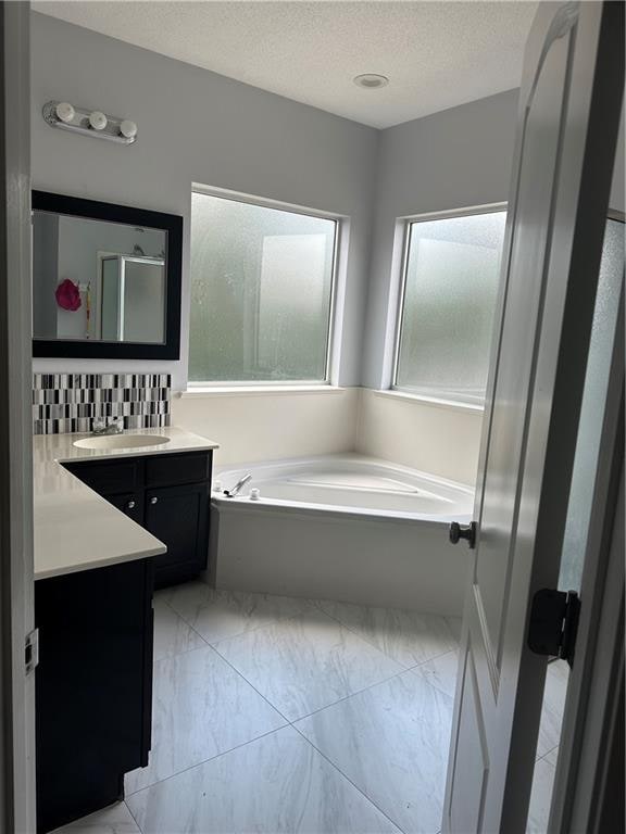 bathroom with backsplash, a textured ceiling, independent shower and bath, and vanity