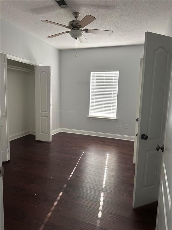 unfurnished bedroom with dark hardwood / wood-style floors, a textured ceiling, ceiling fan, and a closet