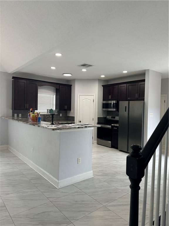 kitchen with light stone countertops, appliances with stainless steel finishes, backsplash, and kitchen peninsula