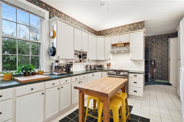 kitchen with ceiling fan, white cabinets, light tile patterned flooring, and stainless steel range with gas cooktop