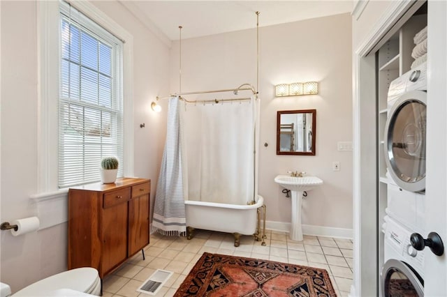 bathroom featuring stacked washer / dryer, a tub to relax in, toilet, and tile patterned floors