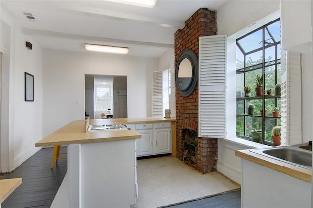 kitchen featuring white cabinetry, white gas cooktop, brick wall, beam ceiling, and hardwood / wood-style floors