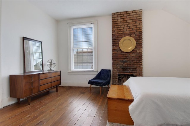 bedroom with vaulted ceiling, hardwood / wood-style flooring, and a fireplace