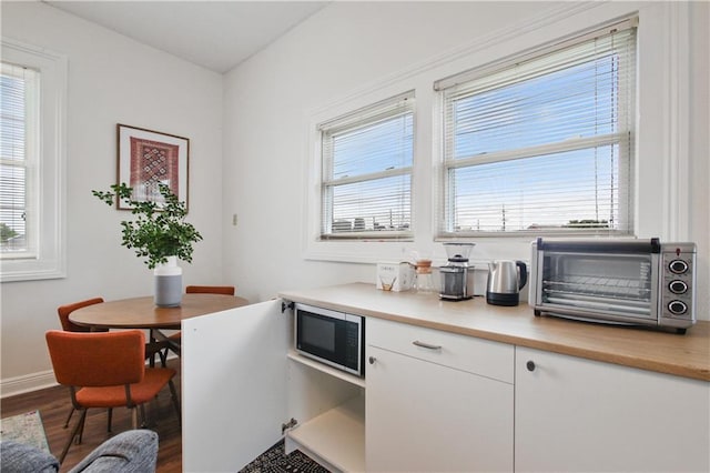 interior space featuring stainless steel microwave, hardwood / wood-style floors, and white cabinetry