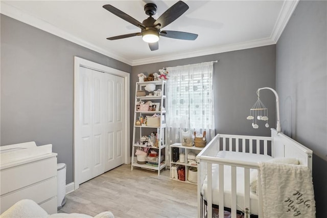 bedroom with light wood-type flooring, ceiling fan, a nursery area, and crown molding