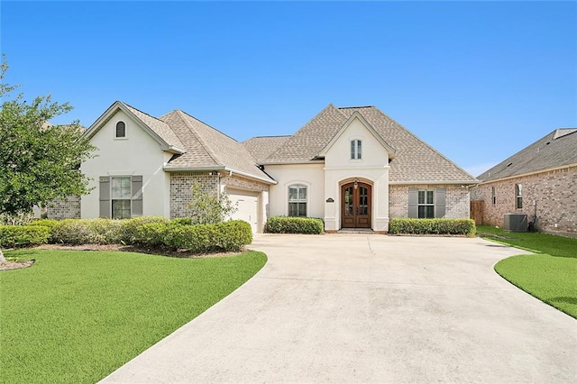 french provincial home with a garage, a front lawn, and central air condition unit