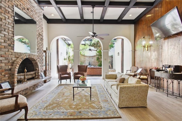 living room featuring ceiling fan, wooden walls, a fireplace, a towering ceiling, and light hardwood / wood-style floors