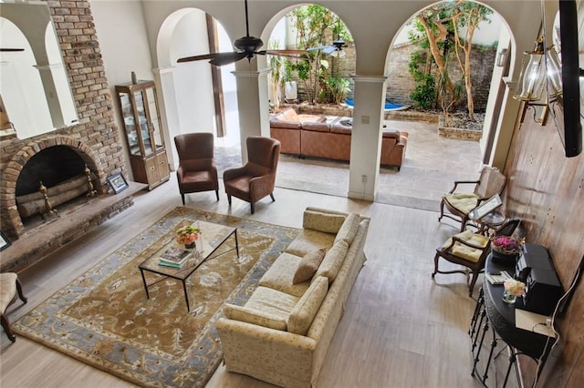 living room featuring ceiling fan, light hardwood / wood-style flooring, a brick fireplace, and a towering ceiling