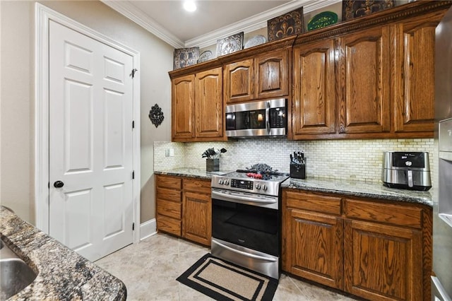 kitchen with appliances with stainless steel finishes, dark stone countertops, ornamental molding, and light tile patterned flooring