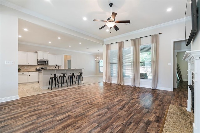 unfurnished living room featuring a premium fireplace, crown molding, light hardwood / wood-style floors, and ceiling fan with notable chandelier