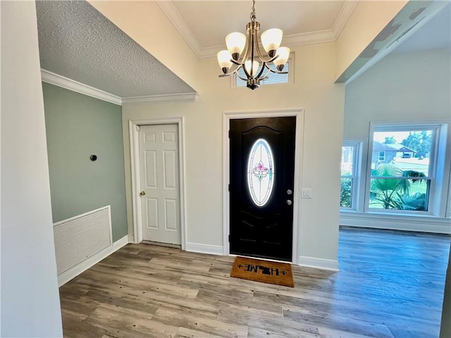 foyer featuring wood-type flooring, a chandelier, a textured ceiling, and crown molding