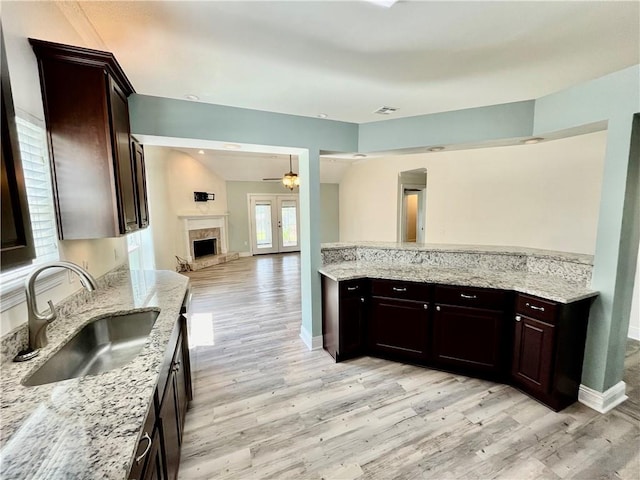 kitchen with light wood-type flooring, light stone countertops, sink, and ceiling fan