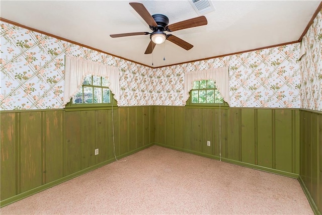 carpeted empty room with a healthy amount of sunlight, wood walls, and ceiling fan