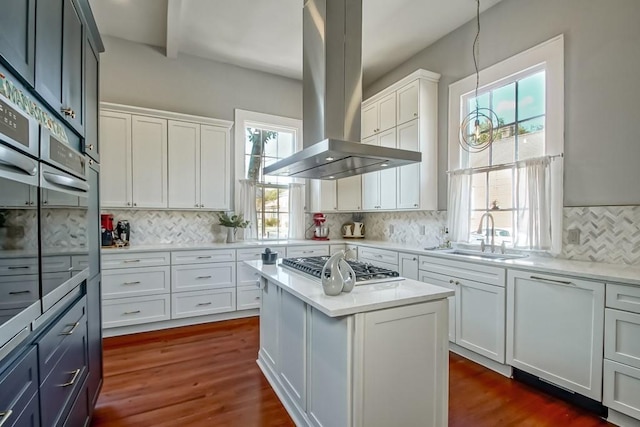 kitchen featuring white cabinets, decorative light fixtures, island range hood, and sink