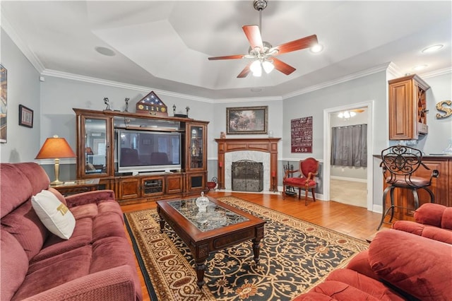 living room featuring a premium fireplace, wood-type flooring, ceiling fan, and ornamental molding