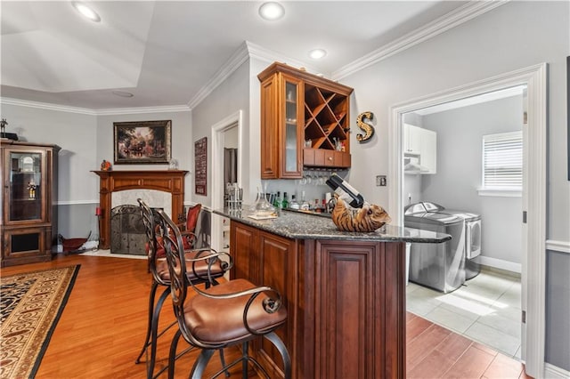 bar with dark stone counters, ornamental molding, light hardwood / wood-style floors, and separate washer and dryer