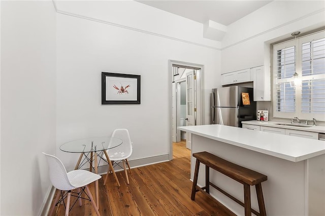 kitchen with white cabinets, sink, dark wood-type flooring, stainless steel refrigerator, and a kitchen bar