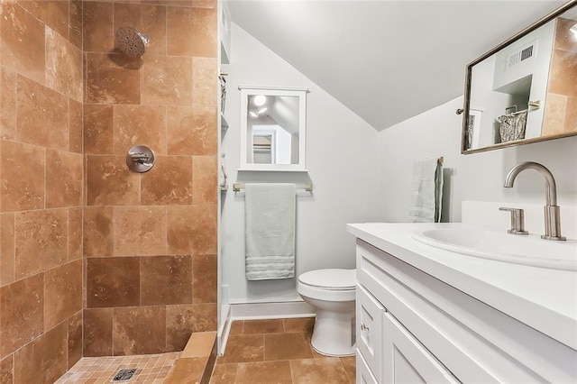 bathroom featuring a tile shower, tile patterned flooring, lofted ceiling, vanity, and toilet