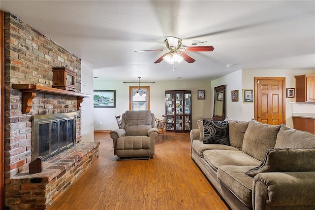 living room featuring a brick fireplace, ceiling fan, and light wood-type flooring